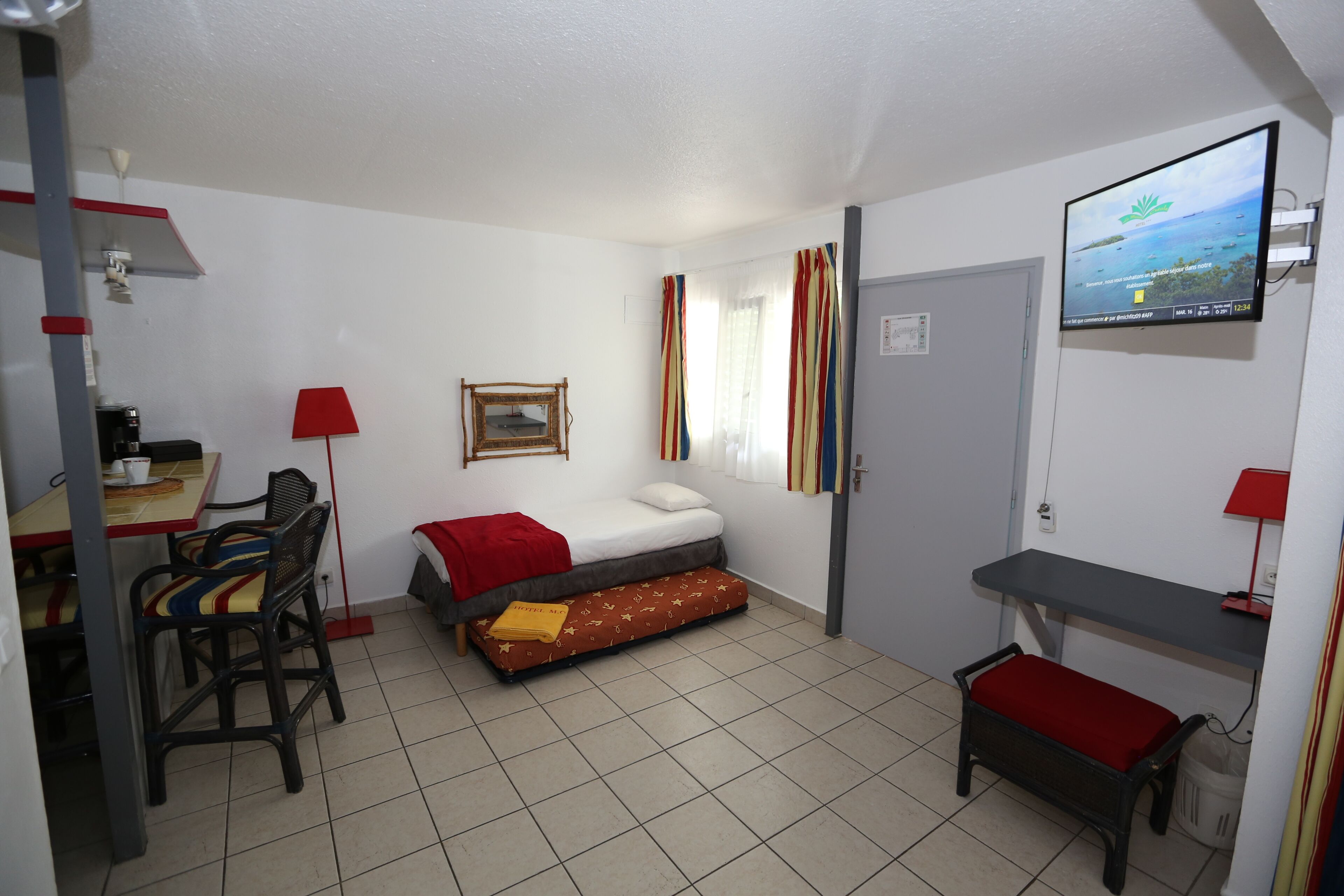 A compact room with a bed, a desk, a chair, a TV, and a window with curtains.