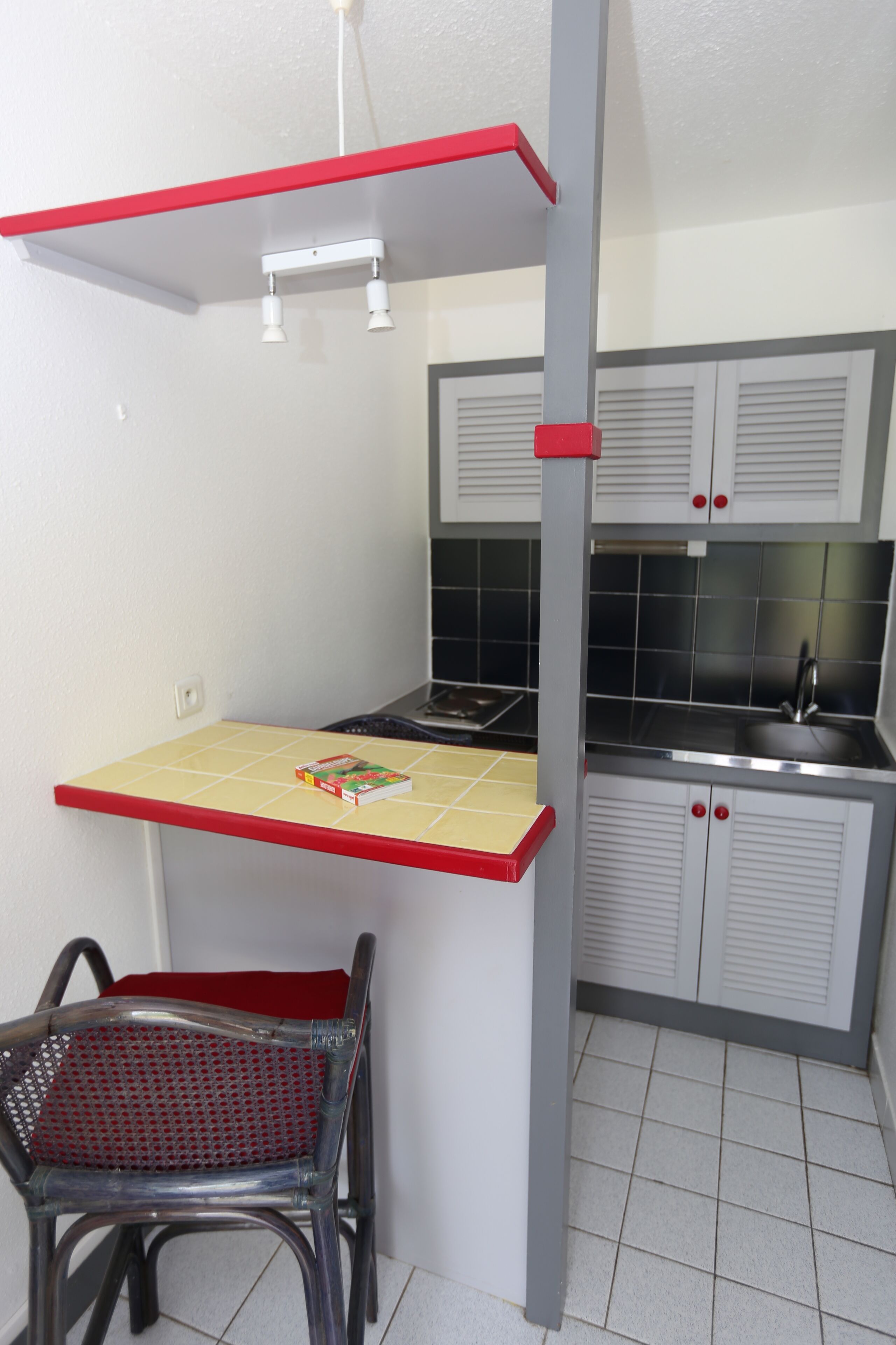 Une cuisine de taille réduite avec un plan de travail rouge, un évier et une chaise.