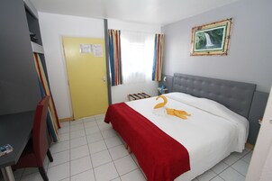 Habitación de hotel con cama, escritorio y silla. Cuenta con una ventana con cortinas, un cuadro en la pared y una puerta.