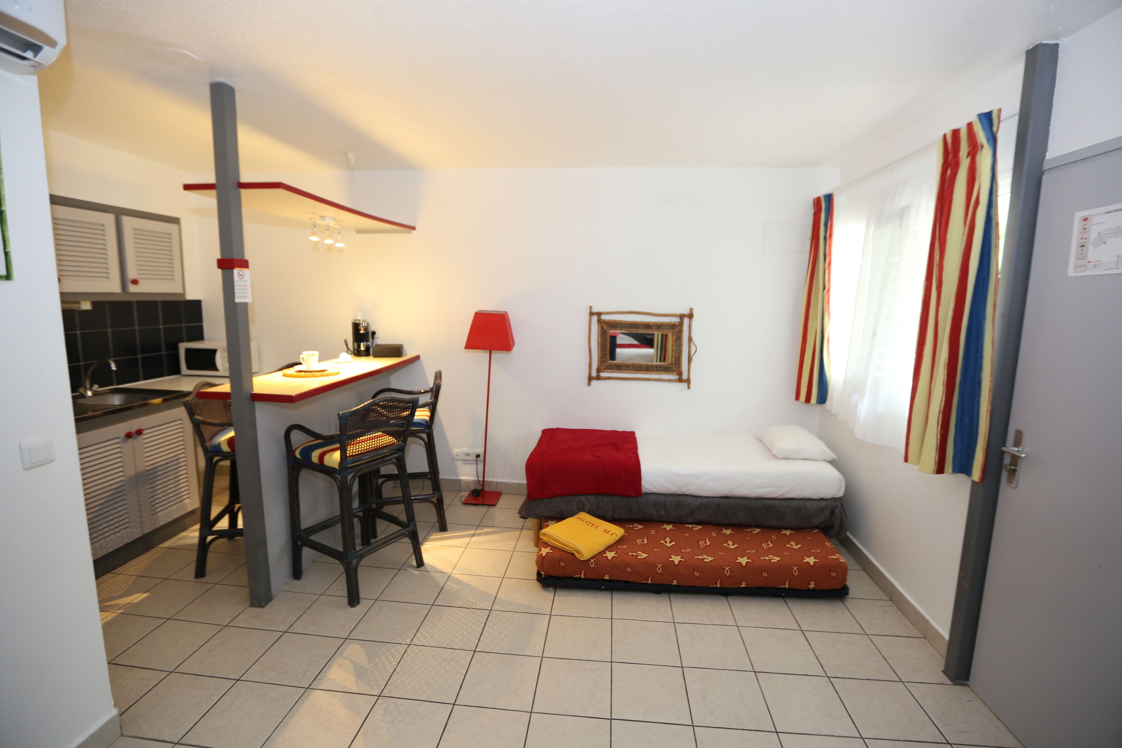 Quarto compacto com cozinha compacta, uma cama, escrivaninha e cadeira.