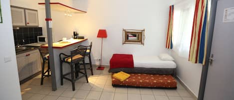 Ein kleines Zimmer mit einer Küchenzeile, einem Bett, einem Schreibtisch und einem Stuhl.