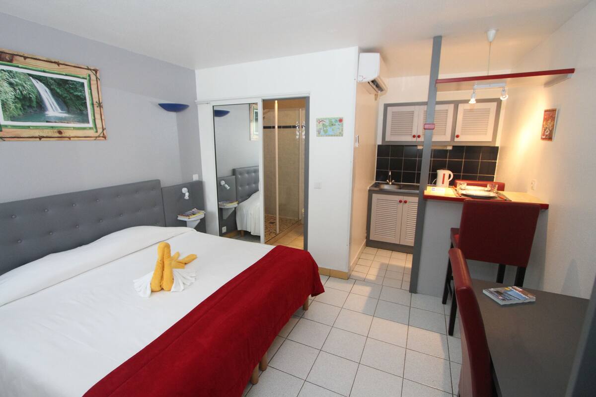 Een hotelkamer met een bed, een klein bureau, een stoel, een badkamer en een kitchenette.