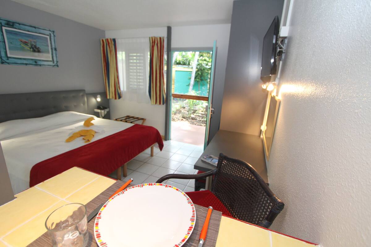Een hotelkamer met een bed, een eettafel met stoelen, een televisie en een raam met gordijnen.