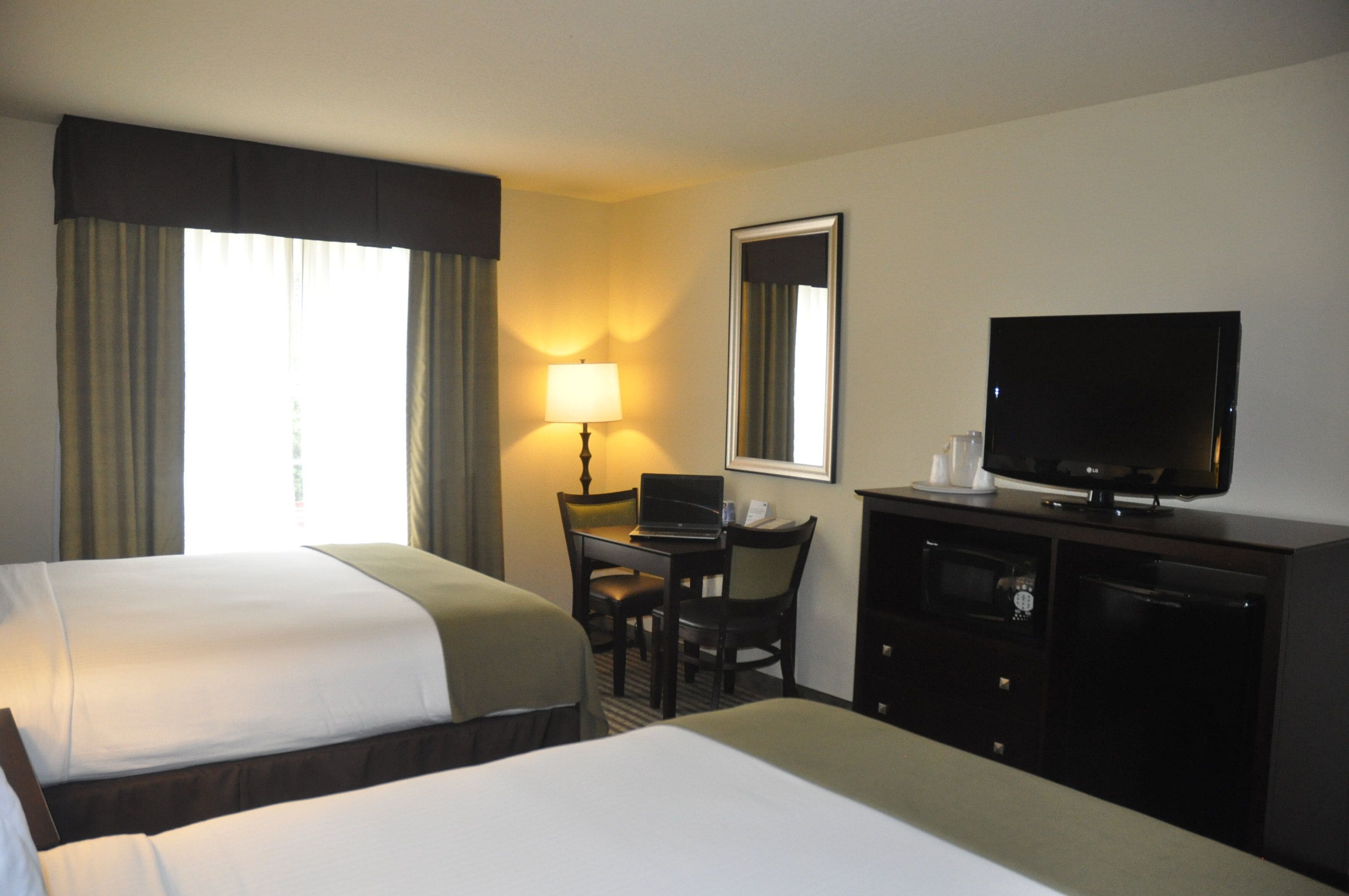 A hotel room with two beds, a desk with a chair, a television, and a microwave.