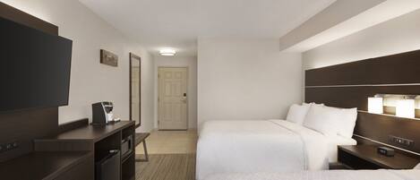 A hotel room with two beds, a desk with a coffee maker, a TV, and a door leading to another room.