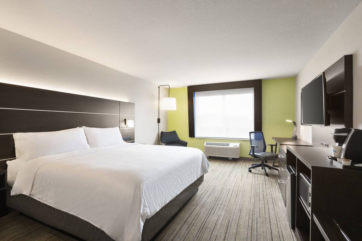 A hotel room with a large bed, a desk with a computer, a chair, and a television.