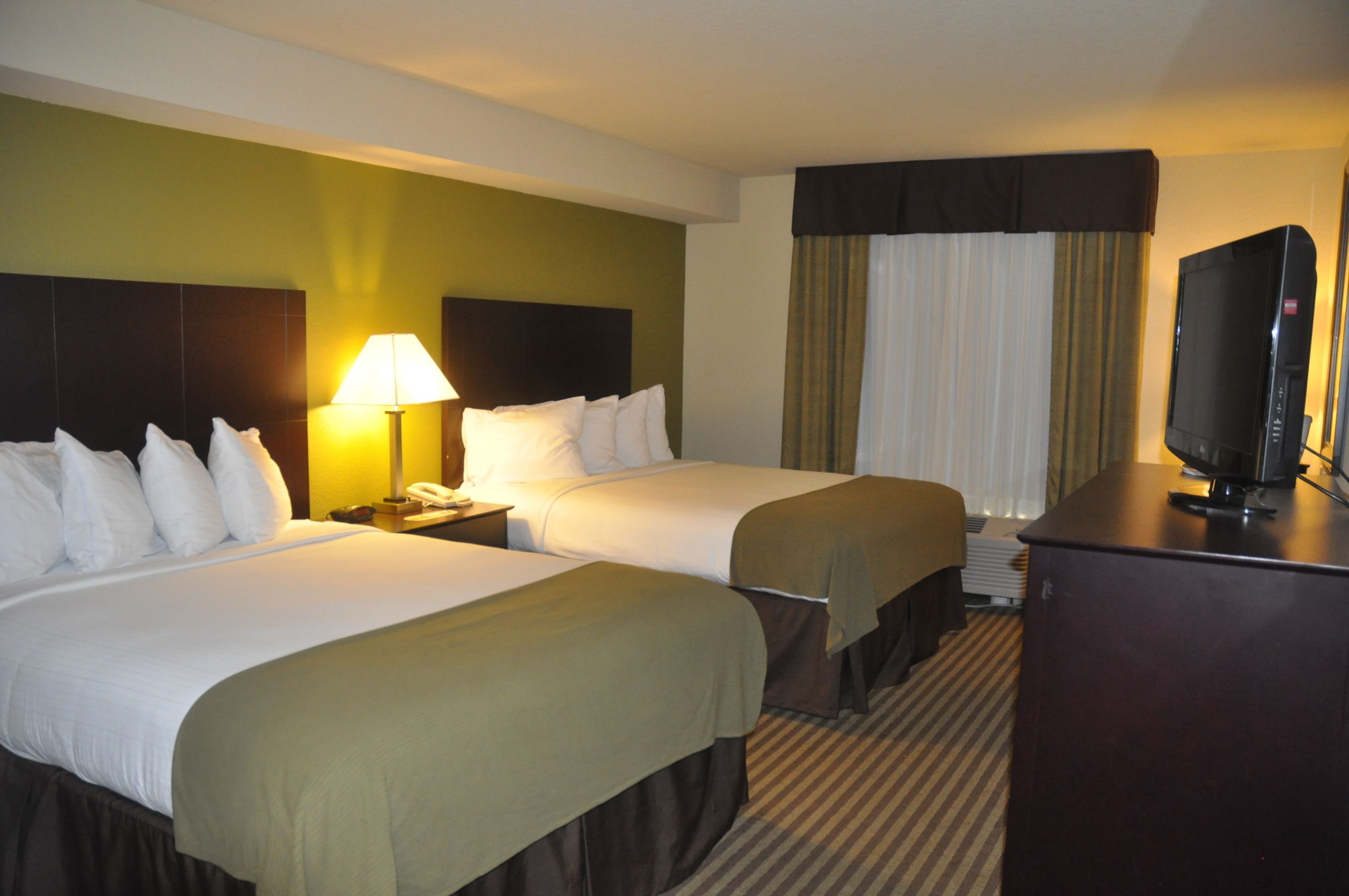 A hotel room with two beds, a TV, a lamp, and a window with curtains.