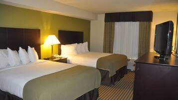 A hotel room with two beds, a TV, a lamp, and a window with curtains.