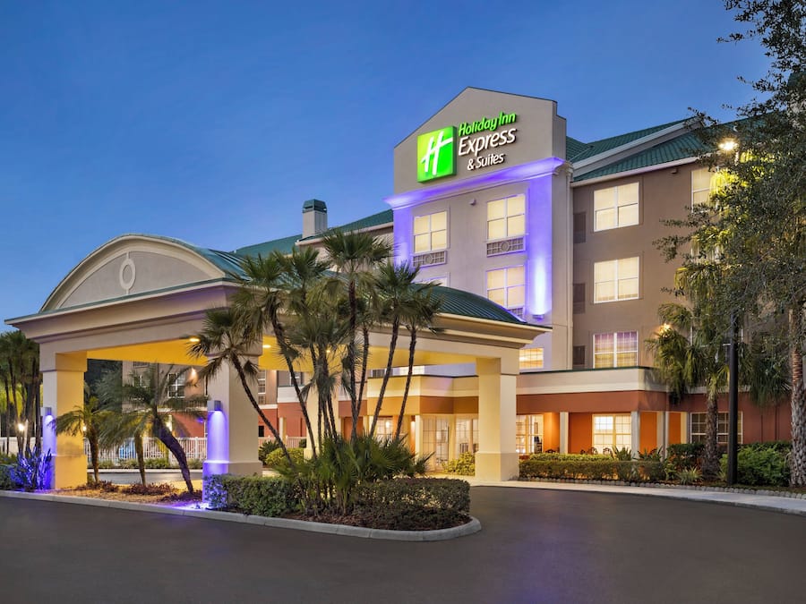 Un hotel Holiday Inn Express con entrada cubierta, palmeras y fachada bien iluminada.