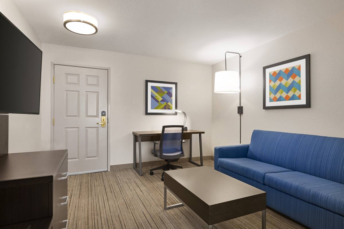 A hotel room with a desk, chair, sofa, and a TV.