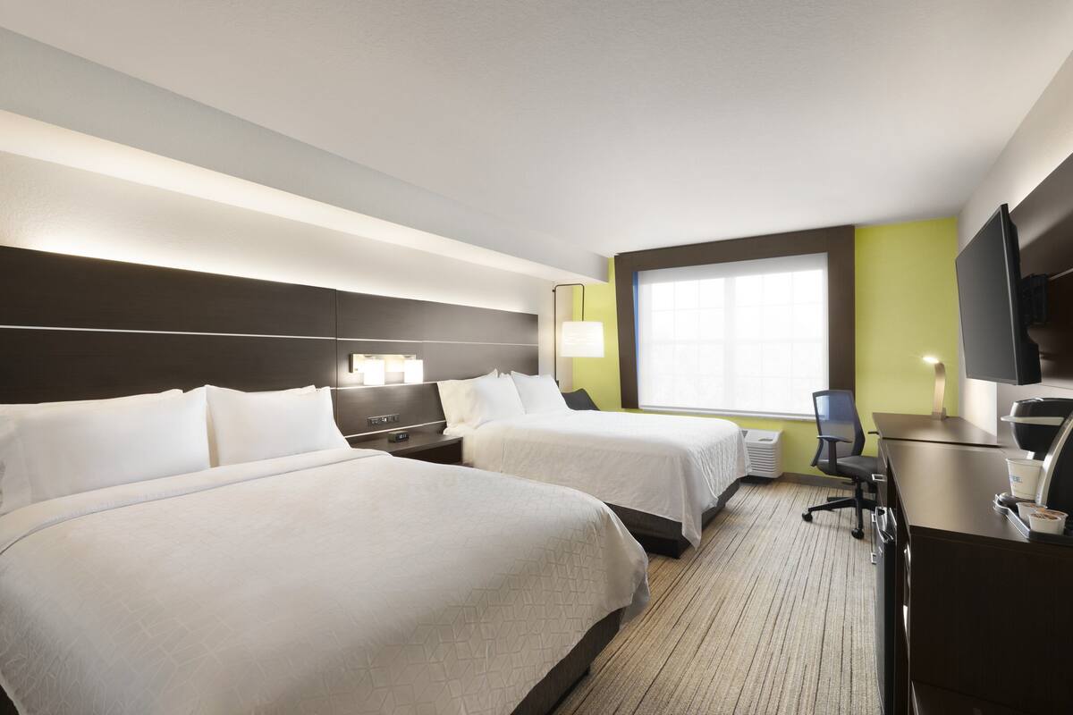 A hotel room with two beds, a desk, a chair, a TV, and a window with blinds.