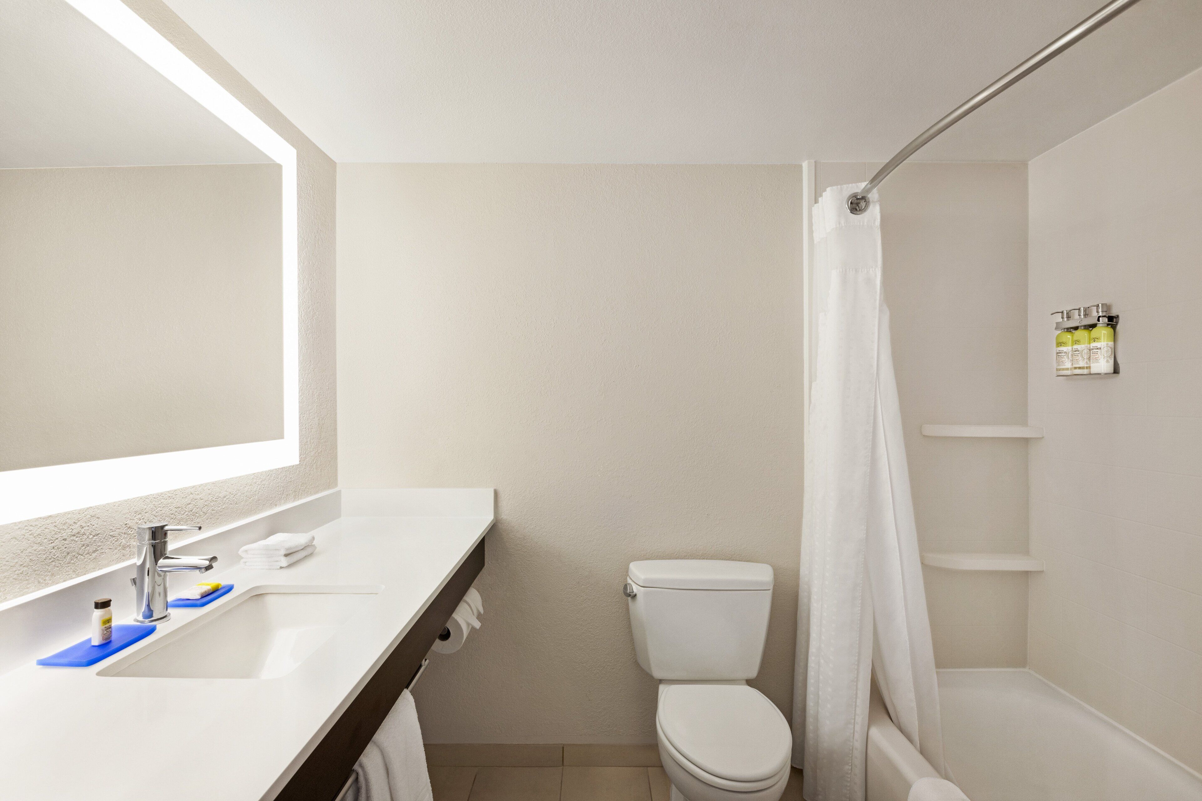 A bathroom with a white sink, mirror, and toilet. There is a shower curtain and a shelf with toiletries.