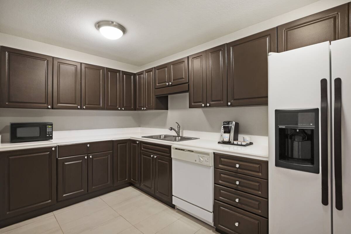 A modern kitchen with dark brown cabinets, a white refrigerator, a built-in dishwasher, and a coffee maker.