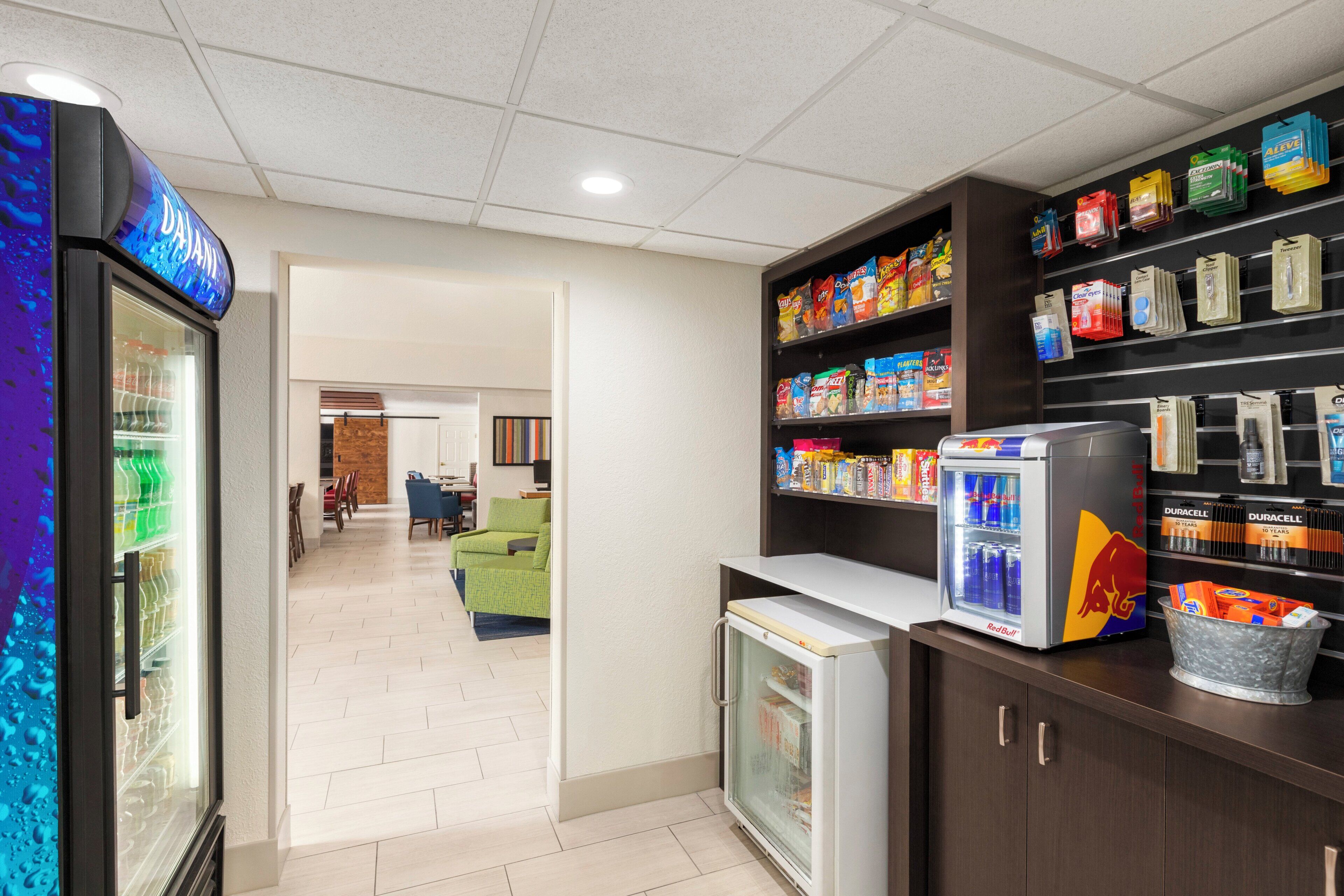 Un hall d’hôtel équipé d’un distributeur automatique, d’étagères remplies d’en-cas, d’un réfrigérateur et d’un espace détente avec des sièges.