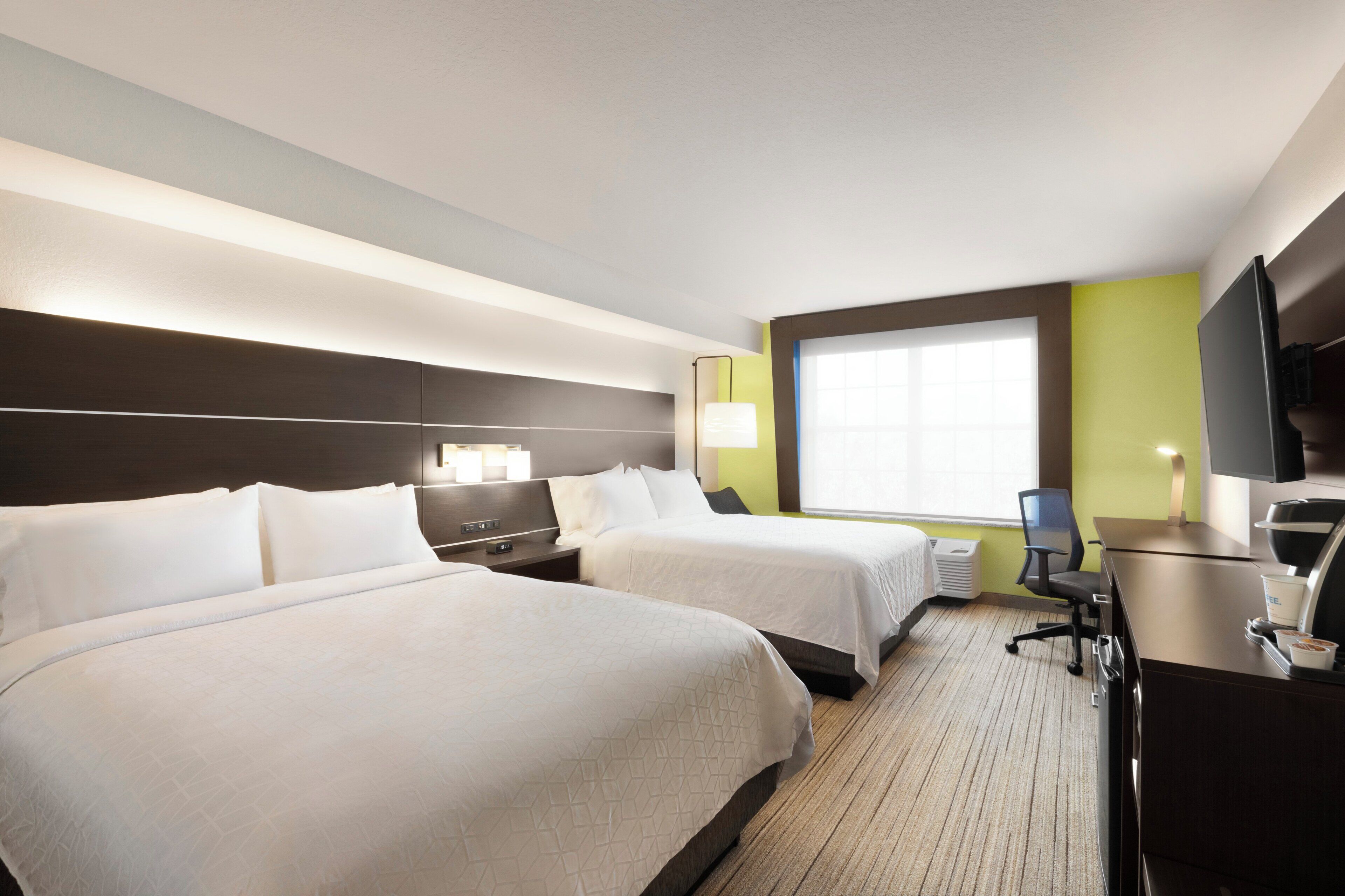 A hotel room with two beds, a desk with a chair, a television, and a window with blinds.