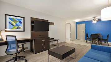 A modern hotel room with a desk, chair, television, and a blue sofa.