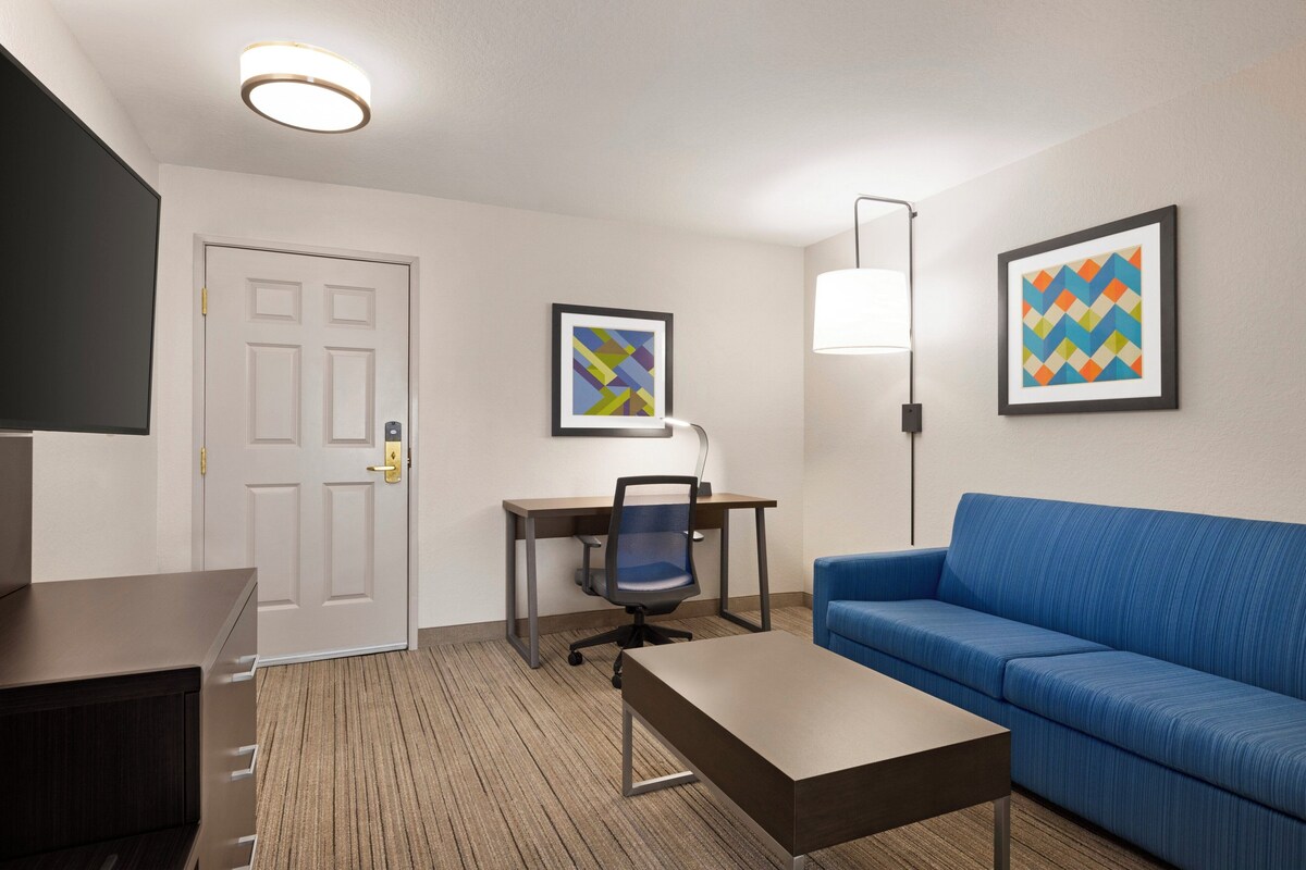 A hotel room with a desk, chair, couch, and a television.