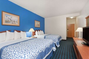 Habitación de hotel con dos camas, televisión, escritorio y alfombra estampada.