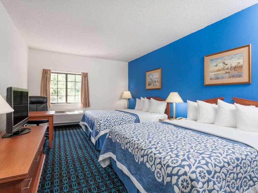 A hotel room with two beds, a desk with a computer, and a window with curtains.