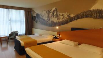 Camera d'albergo con due letti, una scrivania, una sedia, un murale raffigurante montagne e un comodino con una lampada.