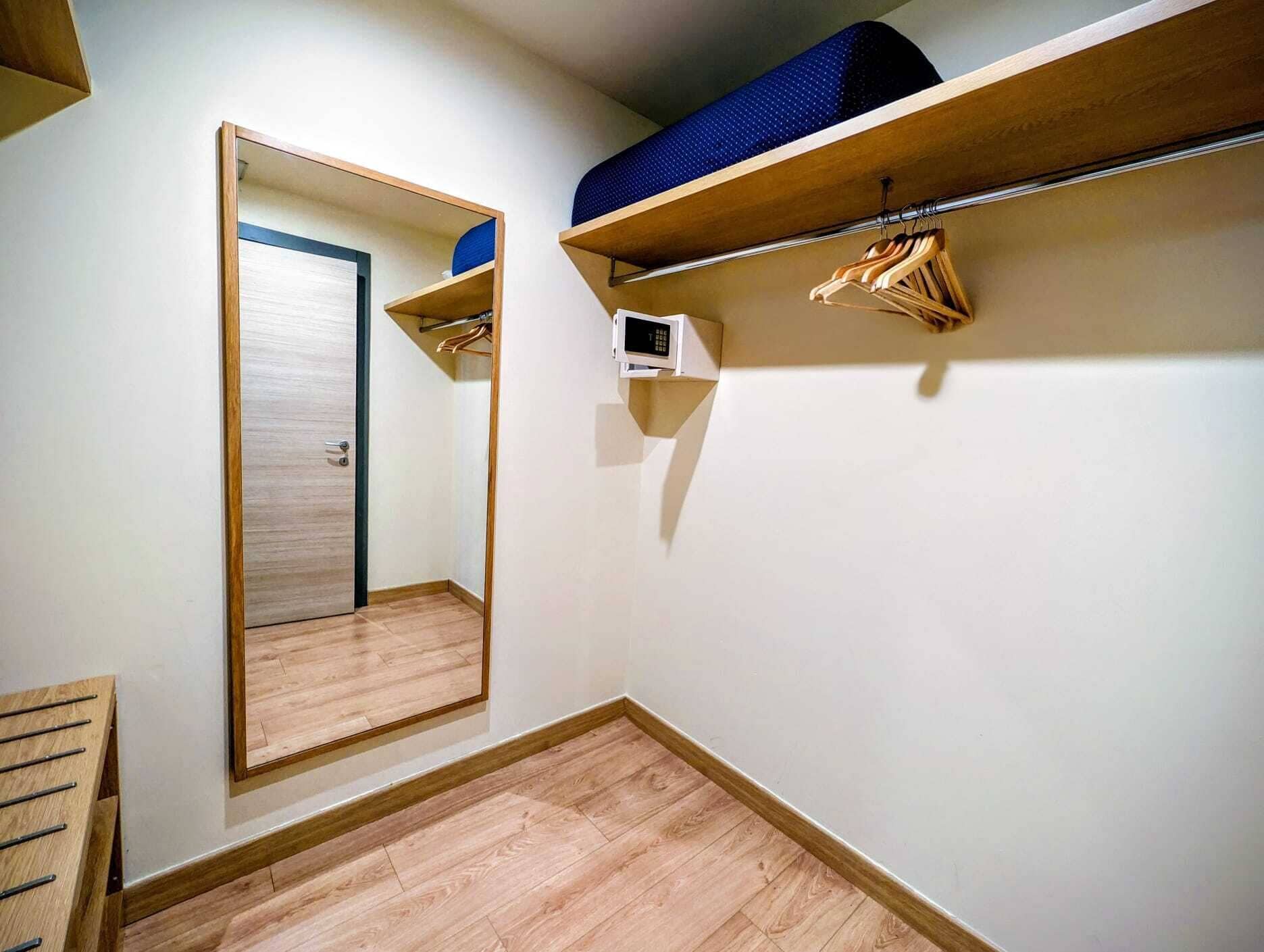 Ein Zimmer mit Holzboden, einem Spiegel, einem Schrank mit Kleidern und einem Regal mit einem blauen Gegenstand.