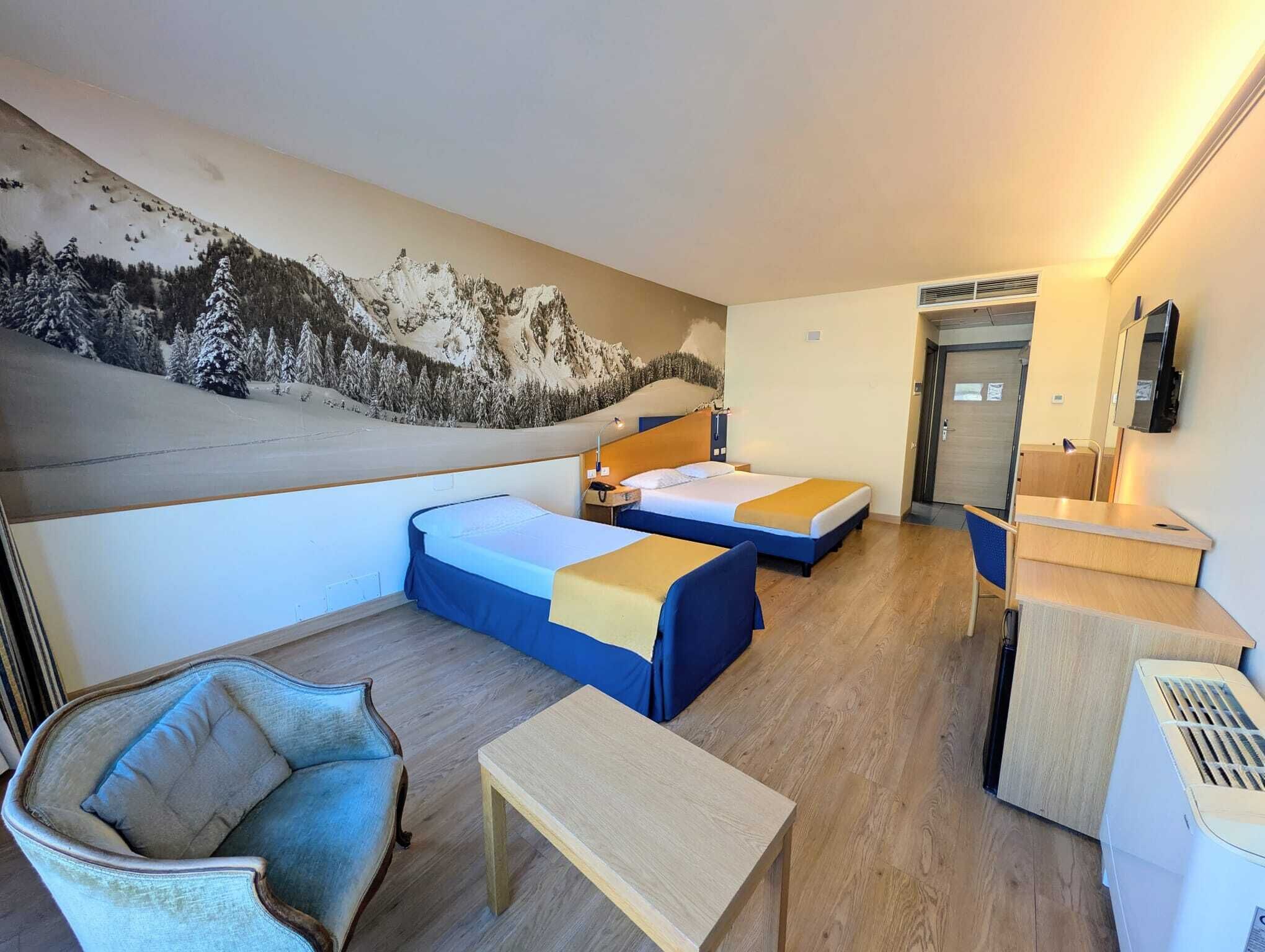 A hotel room with two beds, a desk, a chair, and a large wall mural.