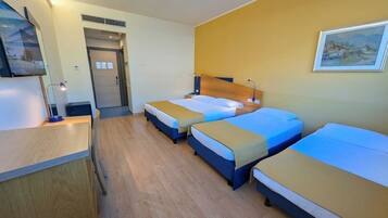 Ein Hotelzimmer mit drei Betten, einem Schreibtisch, einem Fernseher und einem Bild an der Wand.