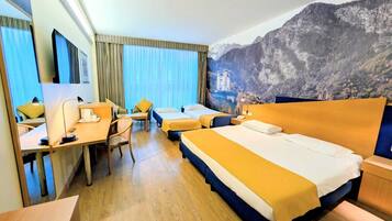 Camera d'albergo con un letto grande, una scrivania e una sedia. Si vede una finestra con tende e un murale raffigurante una montagna sulla parete.
