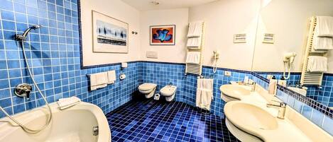 Un baño con paredes de azulejos azules, una bañera, dos inodoros y un lavamanos.