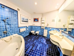 A bathroom with blue tiled walls, a bathtub, two toilets, and a sink.