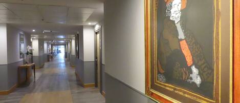 Un pasillo con un retrato enmarcado en la pared, puertas a la derecha y suelo cubierto de alfombra.