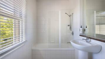 Ein modernes Badezimmer mit einer gläsernen Duschkabine, einem weißen Waschbecken und einem Fenster mit Jalousien.