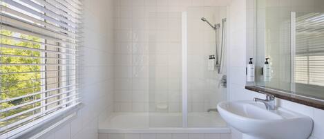 A modern bathroom with a glass-enclosed shower, a white sink, and a window with blinds.