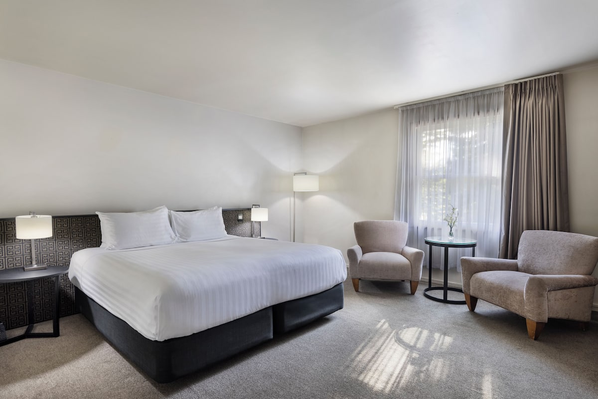 A hotel room with a large bed, two armchairs, a small table, and a lamp.