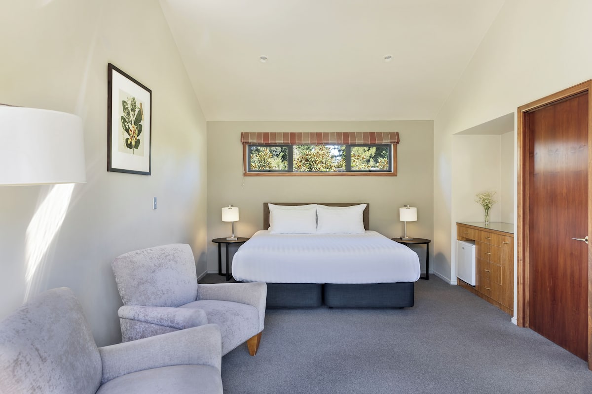 A bedroom with a bed, two bedside tables, a chair, a dresser, and a window with a view of trees.