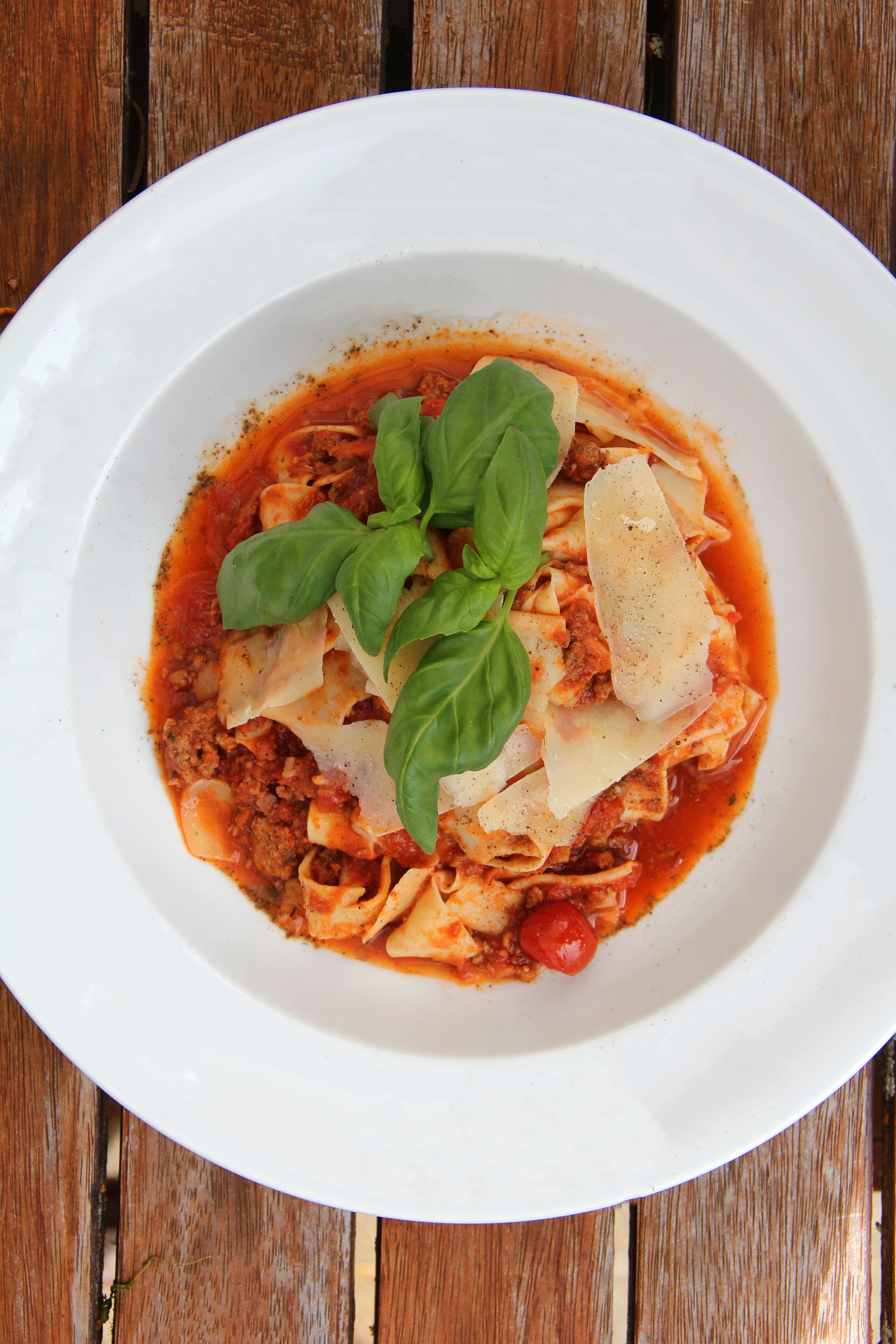 A white plate of pasta with tomato sauce, cheese, and basil on a wooden table.