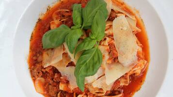 A white plate of pasta with tomato sauce, cheese, and basil on a wooden table.