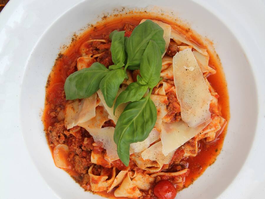 A white plate of pasta with tomato sauce, cheese, and basil on a wooden table.
