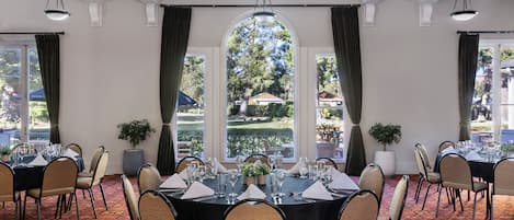 A conference room with round tables, chairs, and a view of a garden through large windows.
