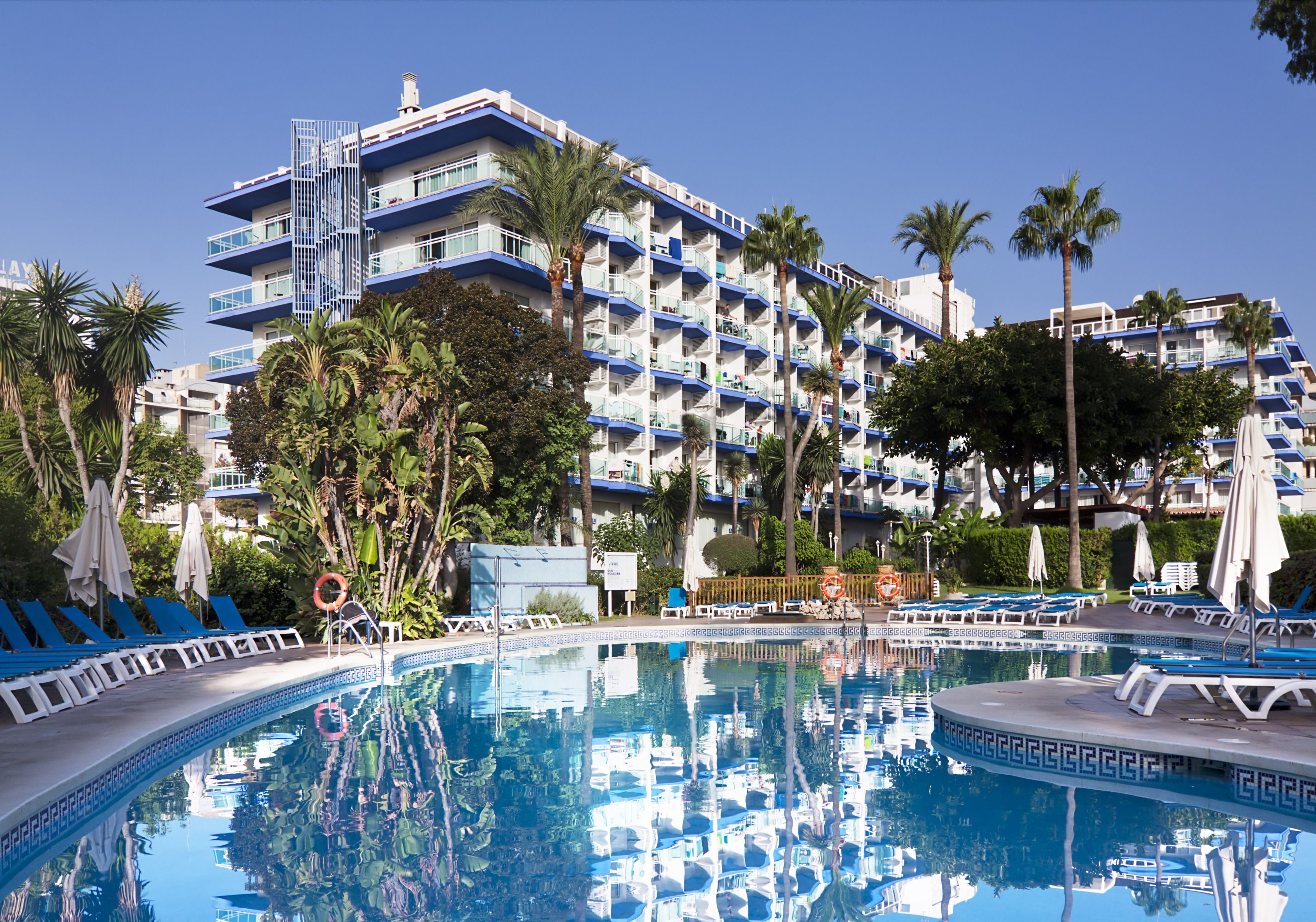 Un hôtel doté d’une piscine, de palmiers et de balcons aux couleurs bleu et blanc.