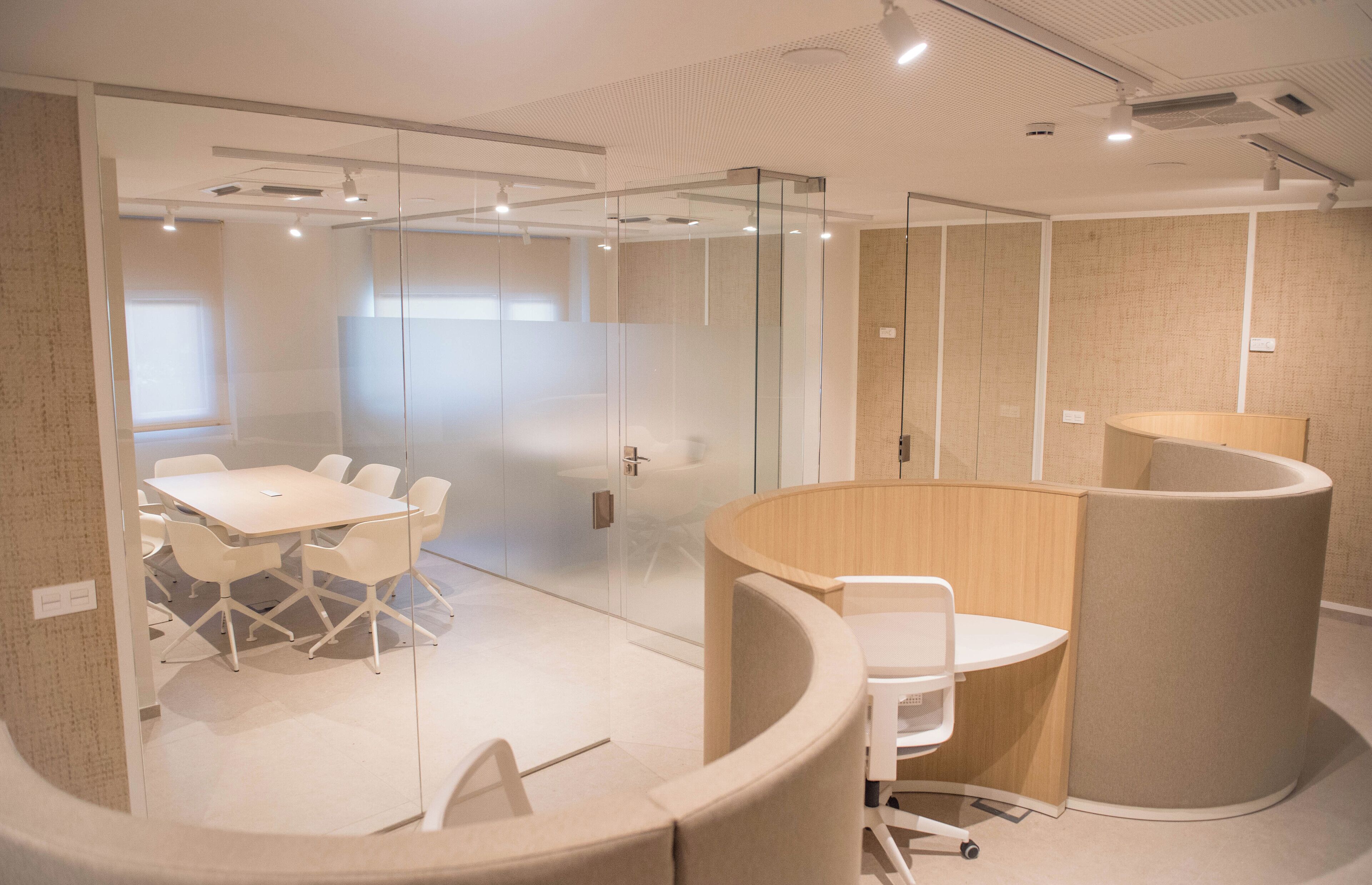A modern meeting room with glass partitions, a round table, and a white conference table.