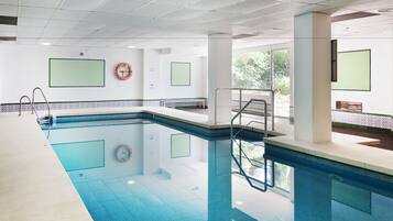 An indoor swimming pool with clear water, a lifebuoy, and a bench.