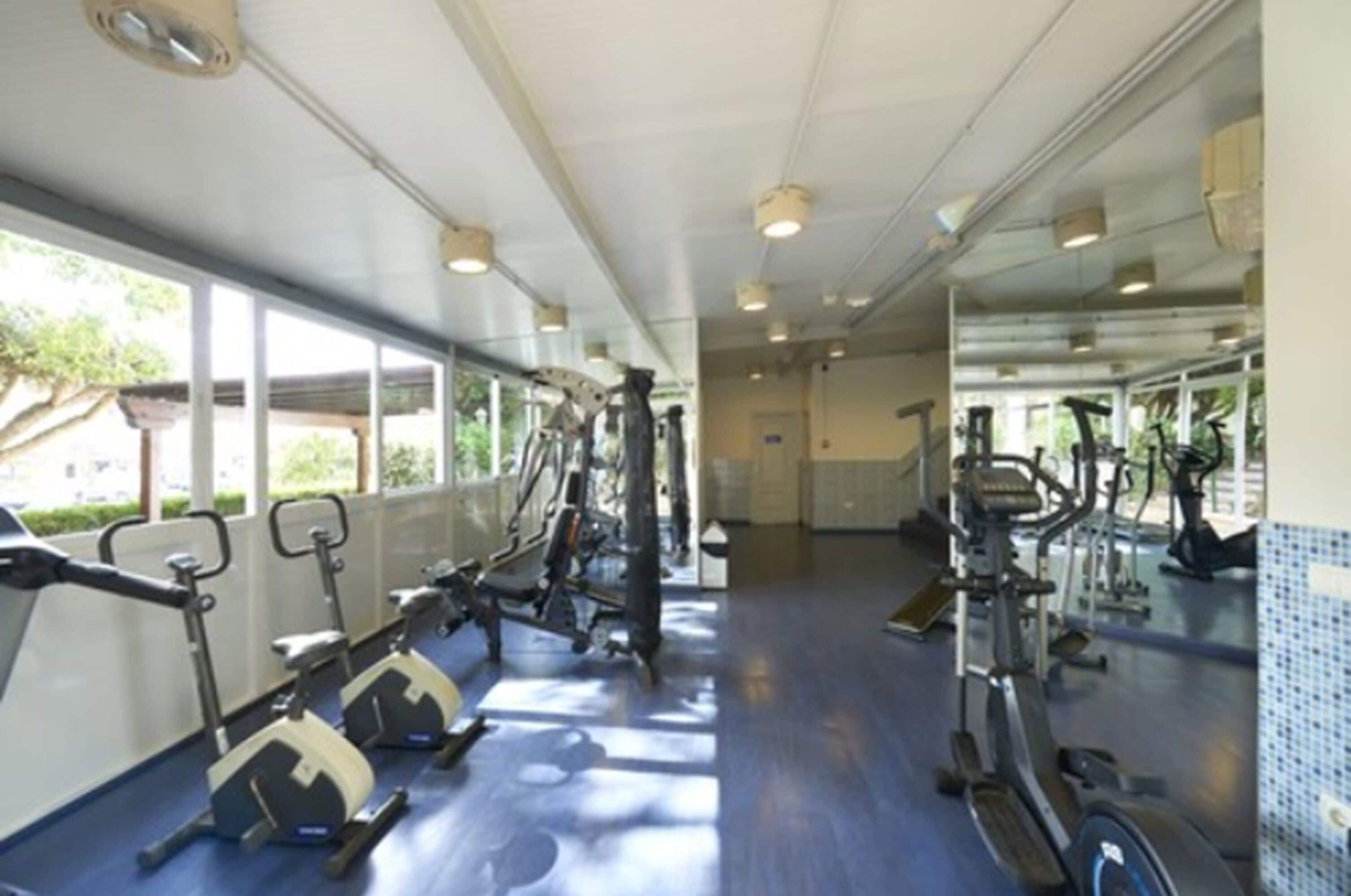 A gym with cardio machines, mirrors, and windows.