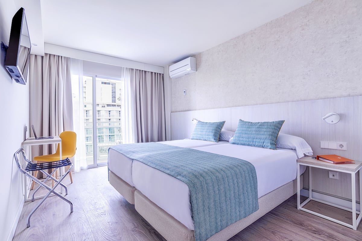 Habitación de hotel moderna con una cama grande, un escritorio con una silla y vistas de la ciudad a través de la ventana.