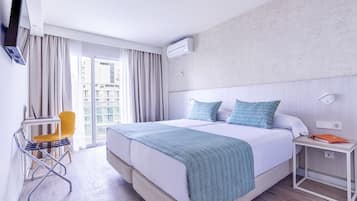 A modern hotel room with a large bed, a desk with a chair, and a view of the city through the window.