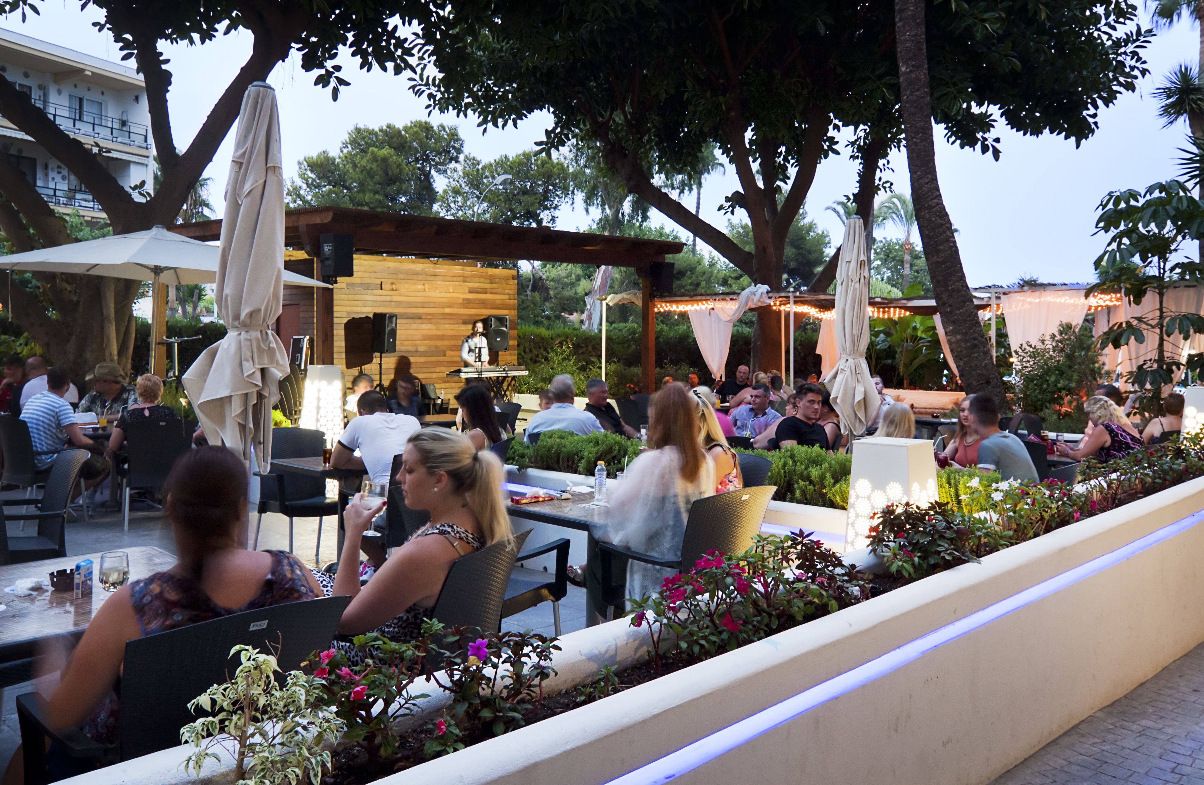 An outdoor dining area with tables and chairs, surrounded by greenery and trees.