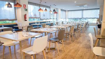 Un comedor moderno con mesas largas, sillas e iluminación colgante.