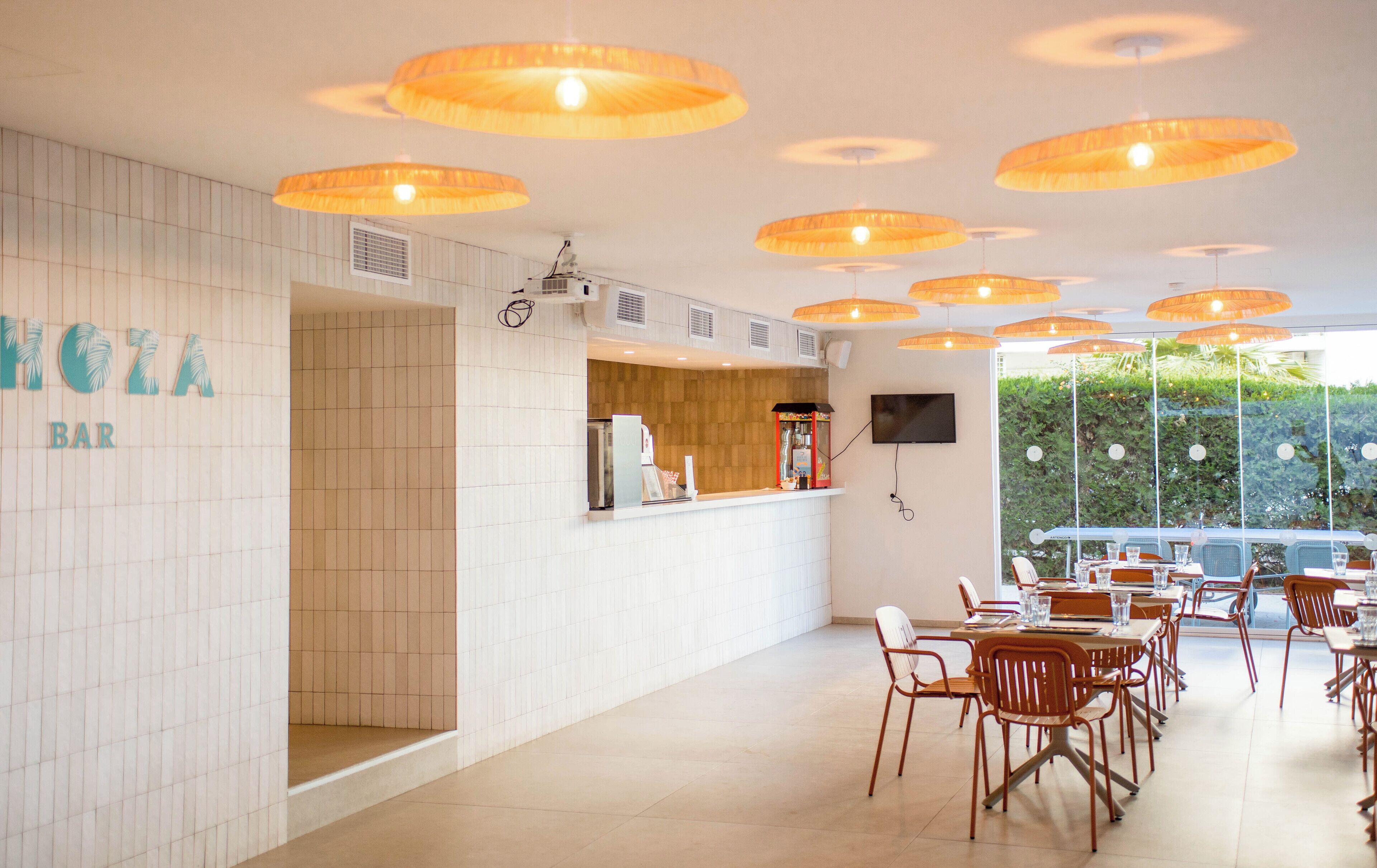 Un espace bar avec un mur recouvert de carreaux, un comptoir et plusieurs lampes oranges suspendues.
