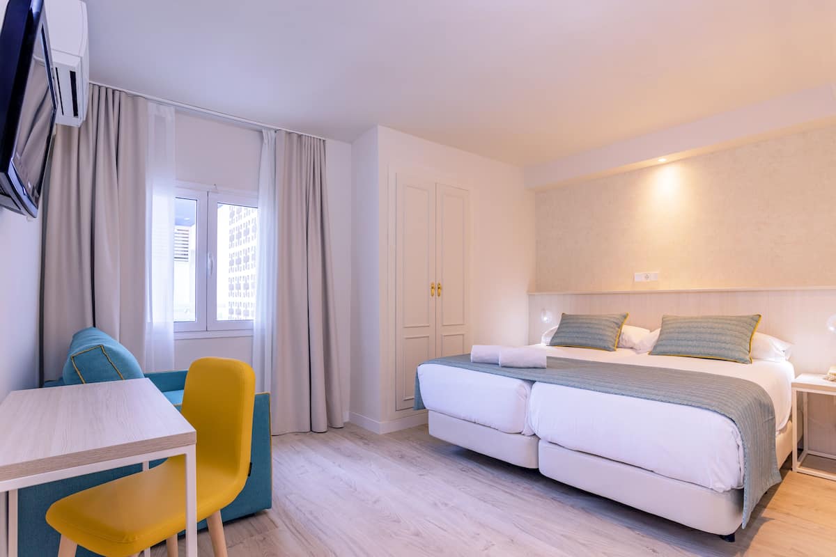 Una habitación de hotel con una cama, un escritorio, una silla y un ventanal con cortinas.