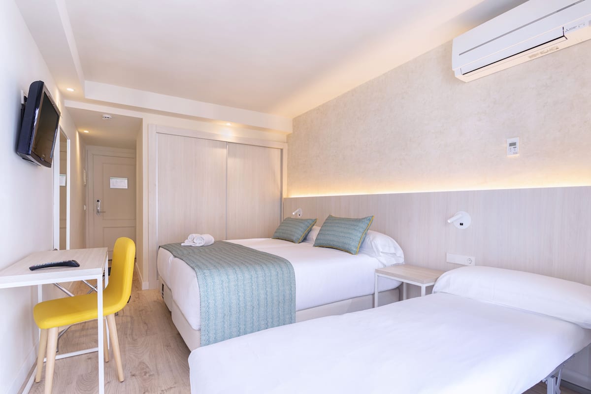 Una habitación de hotel con dos camas, un escritorio con silla, un televisor y aire acondicionado.
